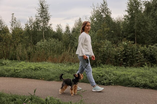 Ragazza teenager in una passeggiata nel parco estivo con il suo animale domestico Yorkshire terrier. Bambino che porta a spasso un cane