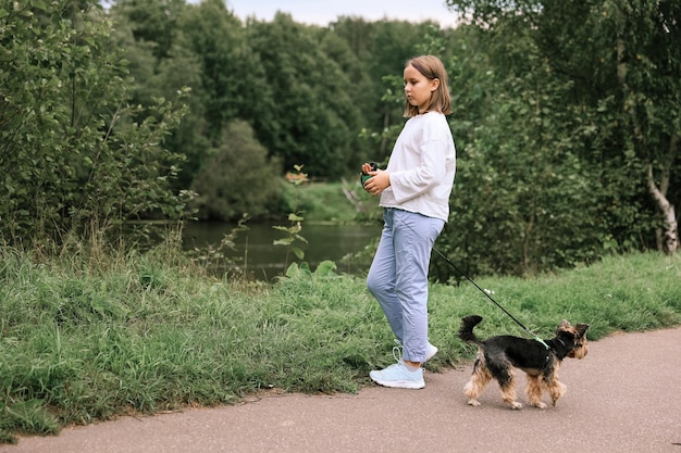 Ragazza teenager in una passeggiata nel parco estivo con il suo animale domestico Yorkshire terrier. Bambino che porta a spasso un cane