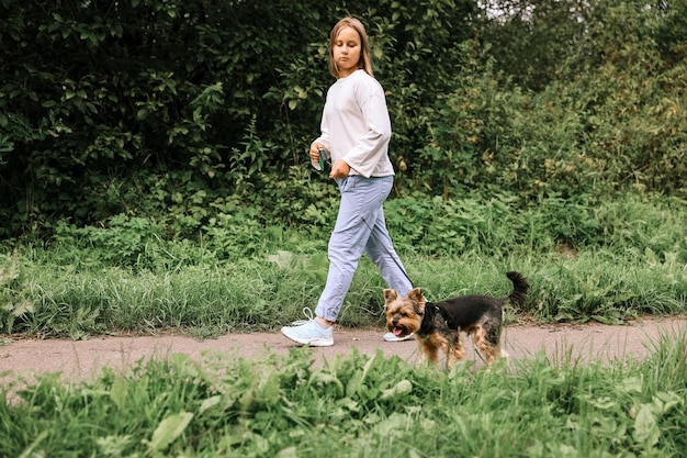 Ragazza teenager in una passeggiata nel parco estivo con il suo animale domestico Yorkshire terrier. Bambino che porta a spasso un cane