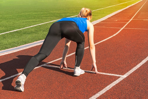 Ragazza teenager nei blocchi di partenza su una pista Incontra Sport ragazza in posa sulla linea di partenza del tapis roulant Stile di vita attivo Concetto di andare avanti