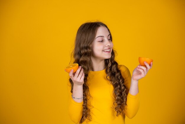 Ragazza teenager positiva tenere frutta arancione su sfondo giallo