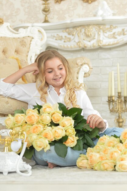 Ragazza teenager riccia sveglia che posa con il mazzo delle rose gialle alla stanza con gli interni dell'annata