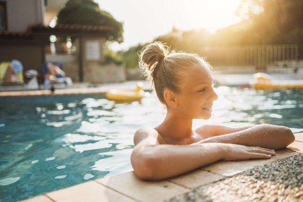 Ragazza teenager sorridente sveglia che gode di una vacanza estiva alla piscina.