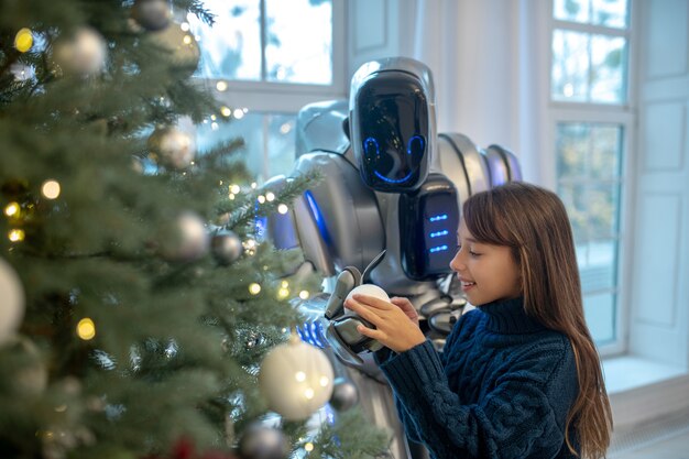 Ragazza teenager sveglia che mette le decorazioni di natale sull'albero