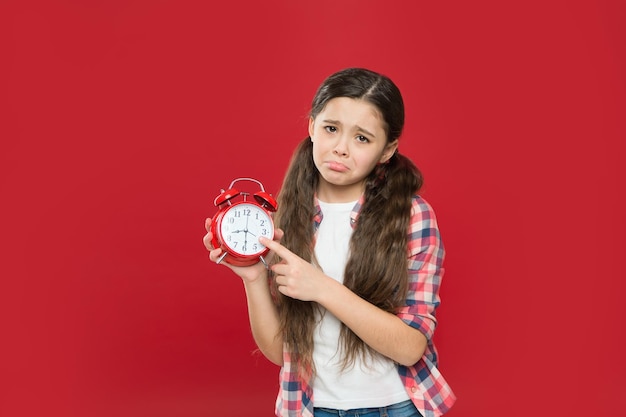 Ragazza teenager triste che punta il dito sul conto alla rovescia della sveglia retrò