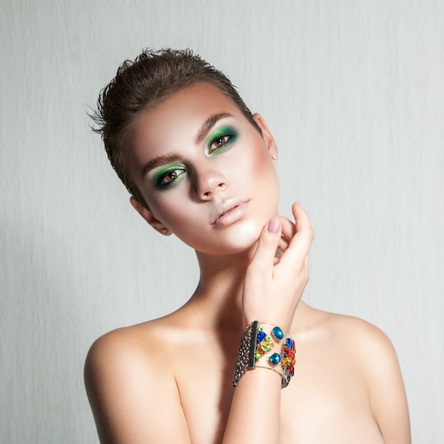 Ragazza tenera con un bel trucco e capelli corti girato in studio su sfondo grigio