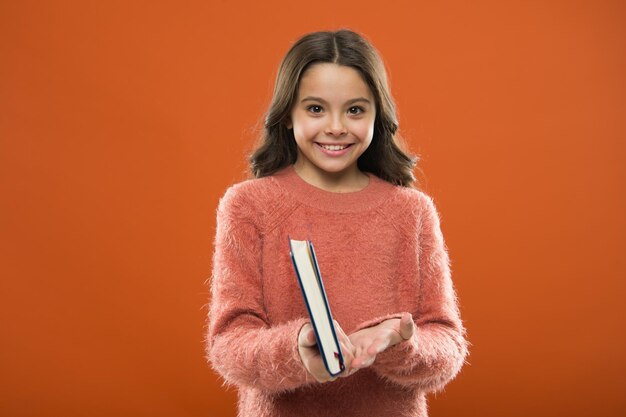 Ragazza tenere il libro leggere la storia su sfondo arancione Il bambino si diverte a leggere il libro Concetto di negozio di libri Meravigliosi libri gratuiti per bambini disponibili da leggere Letteratura per bambini Attività di lettura per bambini