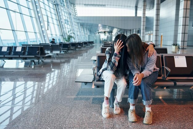 Ragazza triste che piange con la sua amica quando è seduta nell'aeroporto moderno