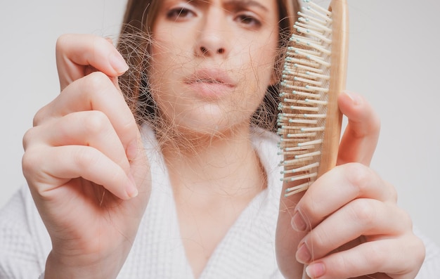 Ragazza triste con capelli danneggiati Trattamento del problema della caduta dei capelli Ritratto di donna con un pettine e capelli problematici