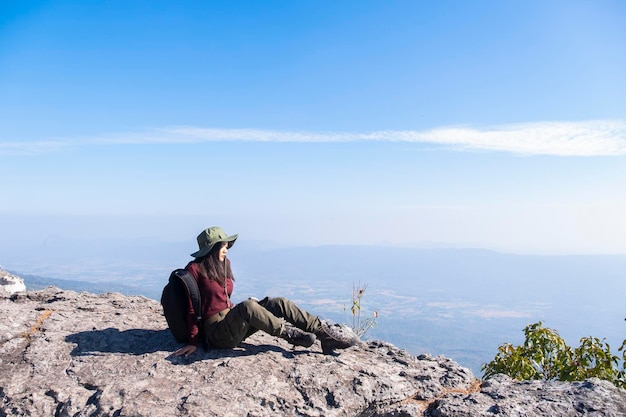 Ragazza turistica che si siede sulla pietra alla montagna che osserva vista panoramica