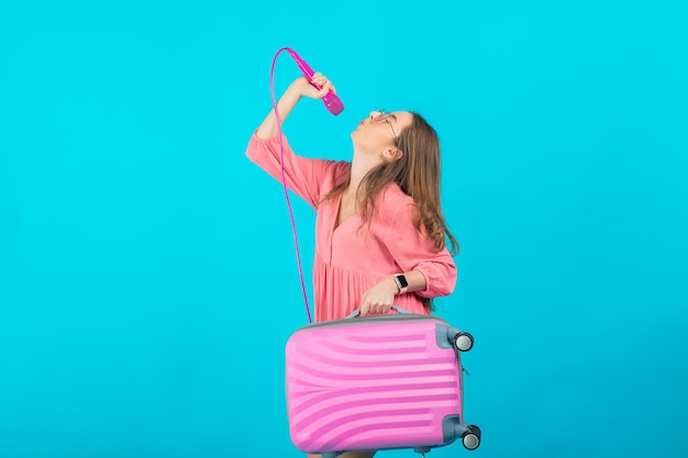 ragazza turistica in un vestito rosa con un microfono rosa su sfondo blu che tiene una valigia rosa