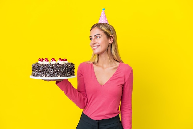 Ragazza uruguaiana bionda che tiene la torta di compleanno isolata su fondo giallo che guarda side