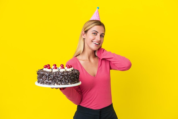 Ragazza uruguaiana bionda che tiene la torta di compleanno isolata su fondo giallo che ride