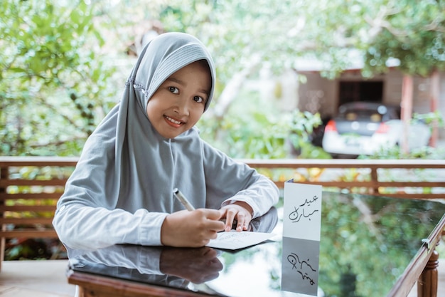 Ragazza velata che sorride scrivendo una cartolina d'auguri felice di eid mubarak