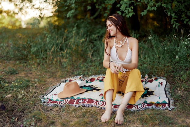 Ragazza vestita come eco hippie rilassante nel parco seduto su una coperta nello stile di vita rilassato al tramonto