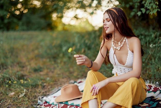 Ragazza vestita come eco hippie rilassante nel parco seduto su una coperta nello stile di vita rilassato al tramonto