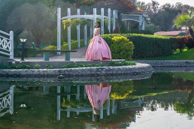 Ragazza vestita da principessa in posa accanto a un ponte e un lago, il suo riflesso è nell'acqua.