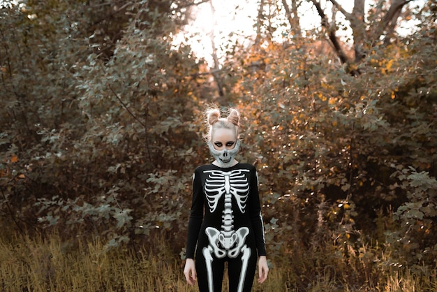 Ragazza vestita da scheletro nella foresta autunnale. Rimase in piedi terribilmente, fissando la telecamera. Halloween