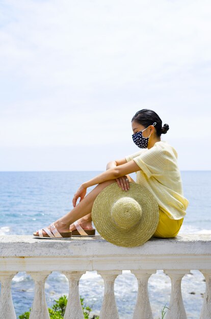 Ragazza vestita in abito giallo con cappello di paglia seduto sulla spiaggia