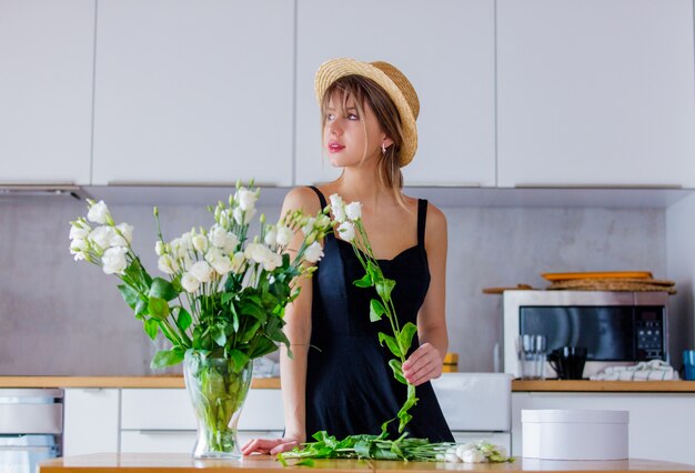 ragazza vestita in un abito nero vicino bouquet di rose bianche in un vaso