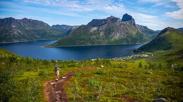 ragazza zaino in spalla escursionismo hesten trailhead che domina la città di fjordgard e possenti montagne, senja