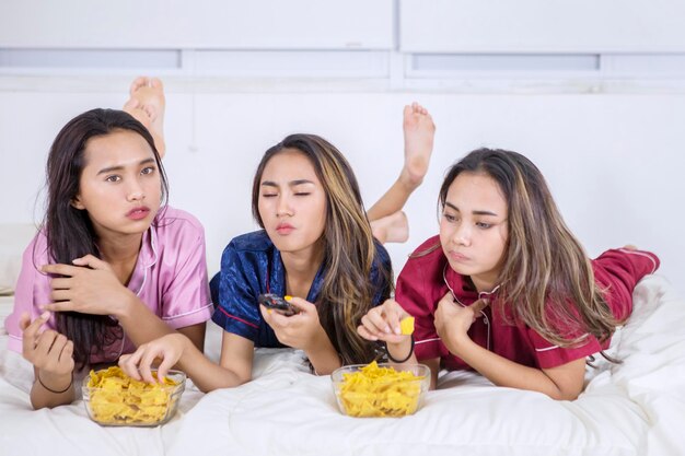 Ragazze adolescenti asiatiche mangiano e guardano la TV a letto.