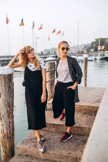 Ragazze bionde in occhiali da sole stanno camminando sul molo sullo sfondo del Lago di Garda, Italia