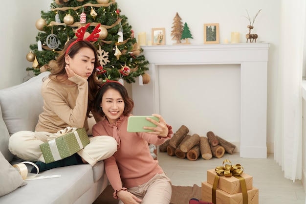 Ragazze carine di Natale che mostrano i regali agli amici del cellulare.