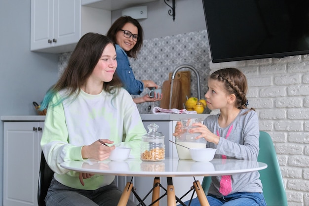 Ragazze che fanno colazione seduti a tavola nella cucina di casa, sorelle adolescenti e bambino di 9, 10 anni che mangia insieme cornflakes con latte