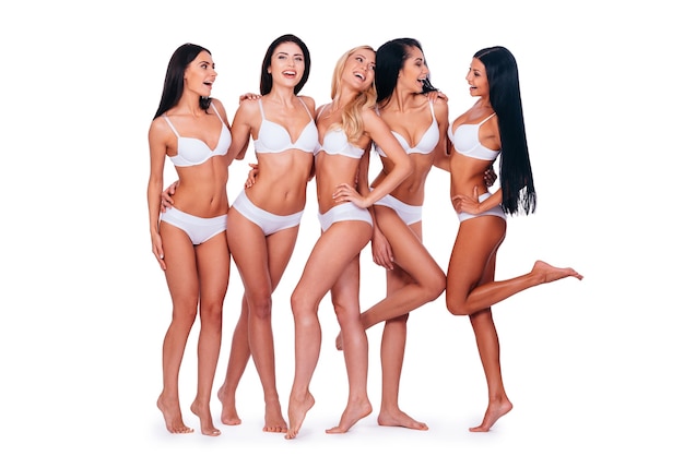 Ragazze che si divertono. Integrale di cinque belle donne in lingerie in posa e dall'aspetto naturale mentre stanno insieme su sfondo bianco