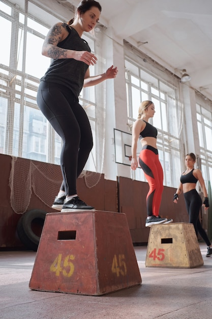 Ragazze che si preparano per l'estate. Giovani donne caucasiche sportive facendo esercizi di salto con attrezzature in un ampio palazzetto dello sport, basso angolo di visione