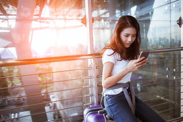 Ragazze che utilizzano lo smartphone per controllare il volo o il check-in online in aeroporto insieme, con i bagagli. Viaggi aerei, vacanze estive o applicazioni per telefoni cellulari