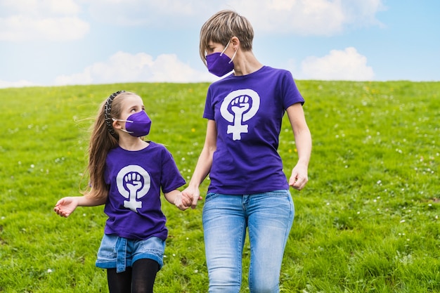 Ragazze di una famiglia che indossano una maglietta viola con il simbolo della donna che lavora che rivendica i diritti delle donne per la Giornata internazionale della donna l'8 marzo e indossano una maschera per il coronavirus