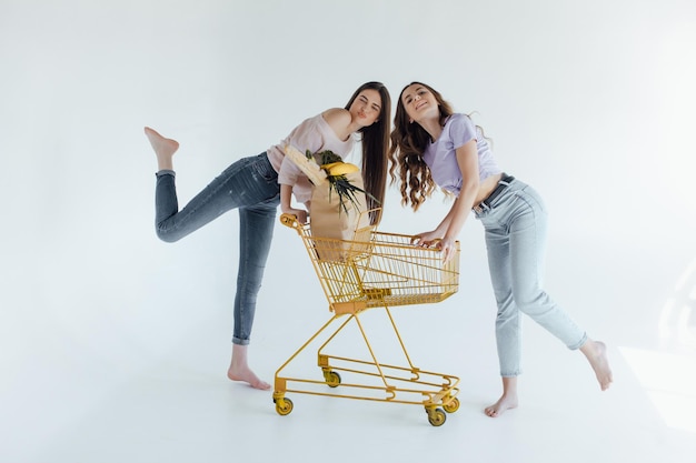 ragazze eccitate con la borsa della spesa seduta nel carrello, isolata on white