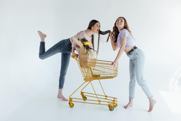 ragazze eccitate con la borsa della spesa seduta nel carrello, isolata on white