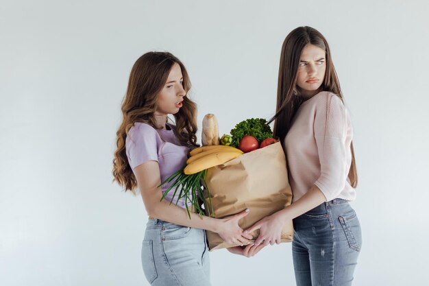 ragazze eccitate con la borsa della spesa seduta nel carrello, isolata on white