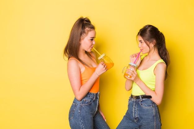 Ragazze felici che sorridono con un drink su sfondo giallo