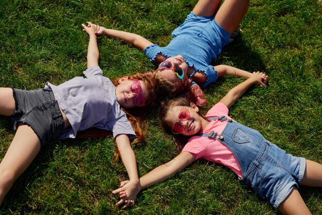 Ragazze felici del bambino in occhiali da sole che si trovano sull'erba nel parco il giorno di estate soleggiato. amicizia e infanzia. vista dall'alto