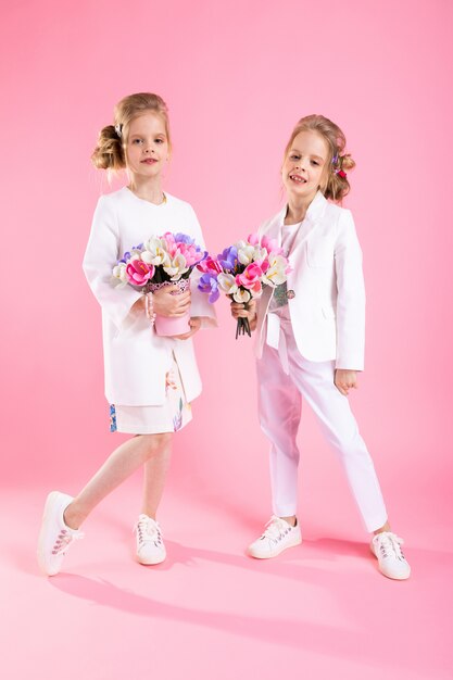 Ragazze gemelle in abiti leggeri con mazzi di fiori stanno su sfondo rosa.