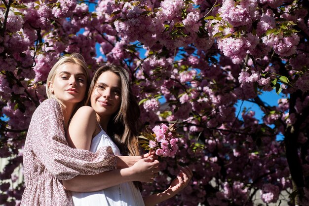 Ragazze in fiori ritratto all'aperto di due giovani belle donne alla moda in posa vicino a fioritura saku