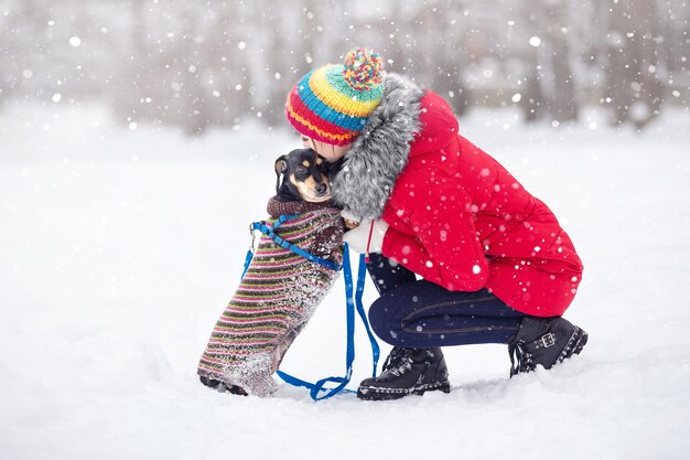 ragazze in giacche calde e cappelli giocano in un parco invernale con un cane a passeggio