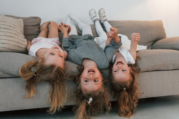 Ragazze sdraiate sul divano a testa in giù e sorridenti Gruppo di bambini è insieme a casa durante il giorno