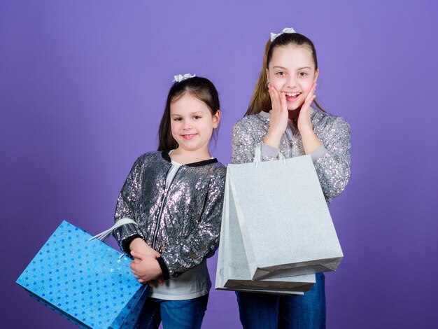 Ragazze sorelle amiche con borse della spesa sfondo viola Shopping e acquisto Black friday Saldi e sconti Giornata dello shopping Bambini pacchetti mazzetto Moda bambini Scopri qualcosa di nuovo