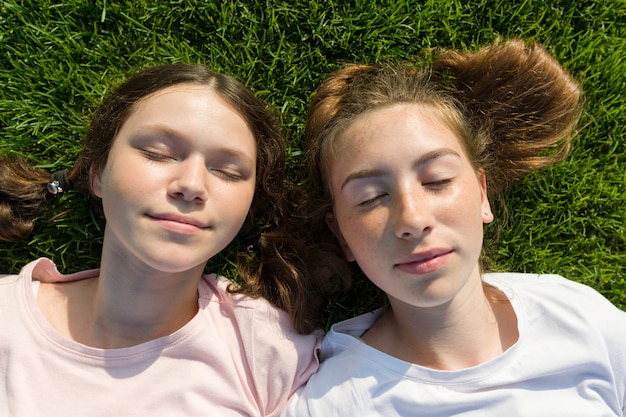 Ragazze sorridenti con gli occhi chiusi che si trovano sull'erba verde.