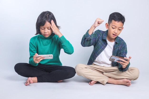 Ragazzi asiatici seduti sul pavimento che giocano a videogiochi competitivi sullo smartphone