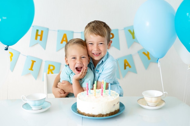 Ragazzi carini per bambini festeggiano il loro compleanno con palloncini blu e una torta di compleanno dolce su sfondo bianco Buon compleanno bambini felici