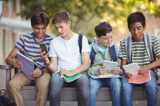 Ragazzi delle scuole utilizzando il telefono cellulare e la tavoletta digitale sul banco