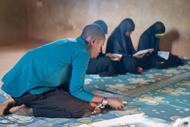 Ragazzi e ragazze adolescenti africani seduti e leggendo un libro in una scuola povera, foto di alta qualità