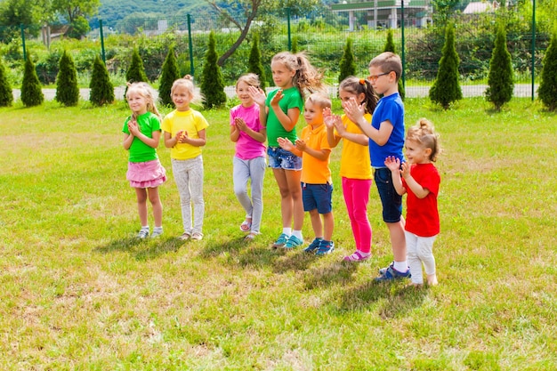 Ragazzi e ragazze felici che battono le mani in piedi sull'erba verde. Animazione campo estivo all'aperto