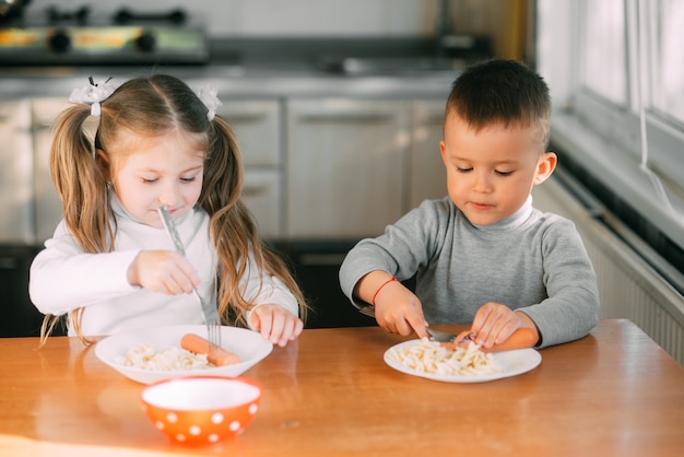 Ragazzi e ragazze in cucina che mangiano salsicce con la pasta è molto divertente e amichevole